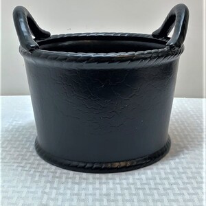 May include: Black planter with two rope handles. The planter has a textured surface and a rope-like trim around the top.