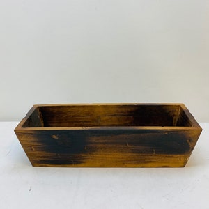 May include: A rustic wooden planter box with a rectangular shape and a dark brown stain. The planter has a slightly distressed look, giving it a vintage feel.