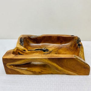 May include: A large, rectangular wooden bowl with a natural, rustic finish. The bowl is carved from a single piece of wood and has a unique, organic shape. The wood is a rich brown color with darker streaks and knots.
