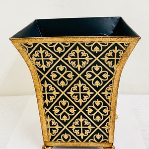 May include: A black and gold metal planter with a geometric pattern and three gold feet.