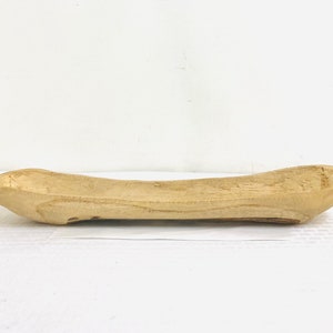 May include: A light-colored, wooden, oblong-shaped bowl. The bowl has a shallow, curved interior and a natural wood grain texture. The ends are pointed, and the sides curve gently upward. The bowl is likely hand-carved and suitable for decorative or functional use.