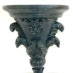 May include: A dark green, ornate, wooden wall shelf with a scalloped top and intricate carvings. The shelf is shaped like a cone with a decorative base.