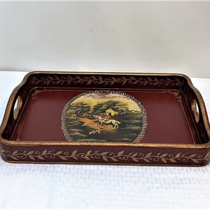 May include: A rectangular wooden serving tray with a dark red base and gold accents. The tray features a painted scene of a rider on horseback in a countryside setting. The tray has two wooden handles on the sides.