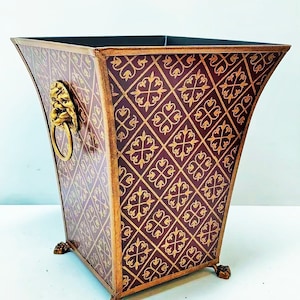 May include: A decorative wastebasket with a burgundy and gold geometric pattern. The metal container has a lion's head ring pull and rests on claw feet. The edges are trimmed in gold.