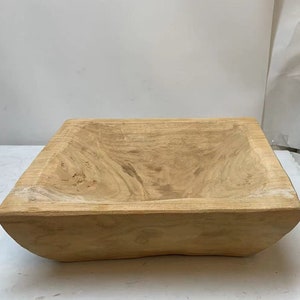 May include: A large, rectangular wooden bowl with a natural wood finish. The bowl is made from a single piece of wood and has a rustic, handcrafted look.