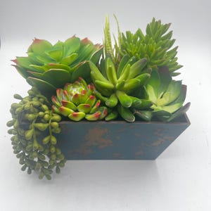May include: A rectangular planter box filled with a variety of artificial succulents. The succulents are various shades of green with red tips, and the planter has a distressed blue-gray finish.