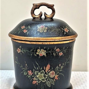 May include: A black ceramic jar with a gold trim and floral design. The jar has a lid with a gold handle.
