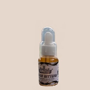 May include: A small, clear glass bottle with a white dropper and cap, filled with a golden liquid. The label reads "King of Bitters" with a crown illustration and botanical information. The bottle is approximately 3 inches tall.