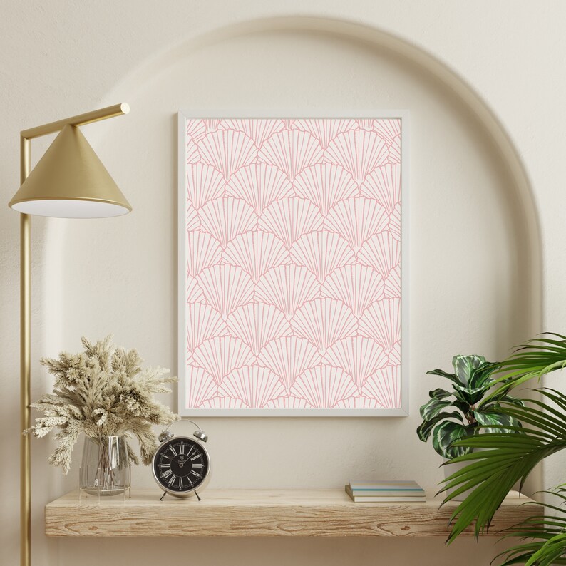 May include: A framed print with a pink and white geometric pattern of overlapping fans. The print is hanging on a white wall above a wooden shelf with a gold floor lamp, a vase with dried flowers, and a silver alarm clock.