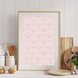 May include: A framed print with a pink and white geometric pattern of overlapping fans. The print is in a gold frame and is hanging on a white wall.