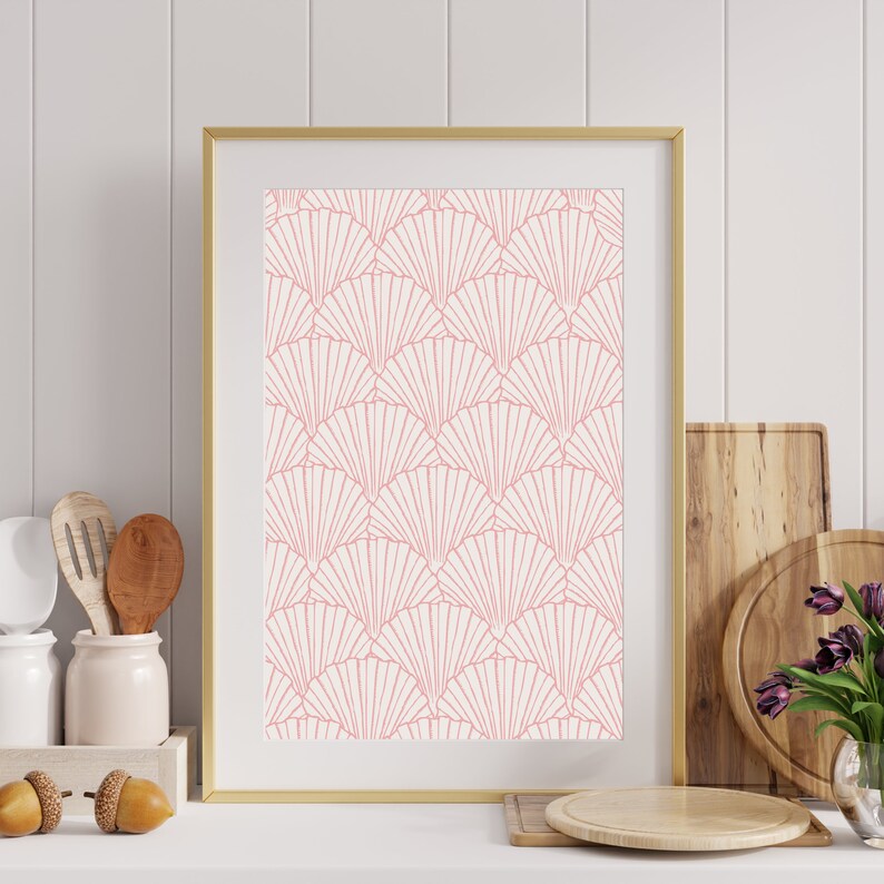 May include: A framed print with a pink and white geometric pattern of overlapping fans. The print is in a gold frame and is hanging on a white wall.