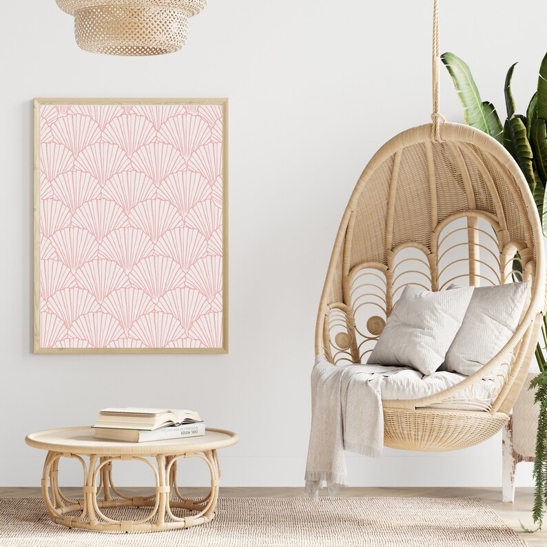 May include: A white wall with a framed print of a pink geometric pattern, a hanging wicker chair with a white throw blanket, and a round wicker coffee table with books on top.