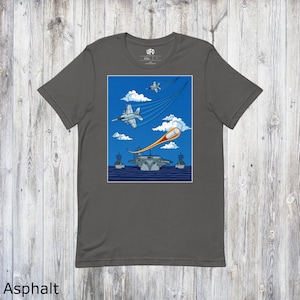 Op de afbeelding: Een donkergrijs T-shirt met een afbeelding van een UFO die een gevechtsvliegtuig boven een vliegdekschip neerhaalt. De tekst "UFO" staat op het label.
