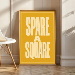 Pode incluir: Um quadro retangular com moldura apresentando um fundo amarelo mostarda com o texto SPARE A SQUARE impresso em letras maiúsculas grandes, em negrito e na cor creme, centralizadas dentro de uma moldura de linha dupla fina.