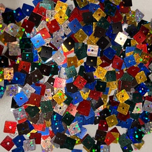 May include: A large assortment of iridescent square sequins in various colors, including red, blue, green, gold, and silver. The sequins have a hole in the center for sewing or attaching.