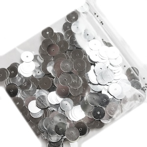 May include: A bag of silver sequins, a type of craft supply used for decorating clothing, accessories, and other items.