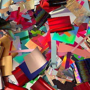 May include: A pile of colorful, iridescent, and metallic paper scraps. The paper is in various shapes and sizes, including squares, rectangles, and strips. The paper is arranged in a random pattern, creating a visually appealing and textured surface.
