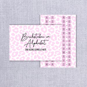 Könnte beinhalten: Zwei rosa Karten mit schwarzem Text und einem Leopardenmuster. Eine Karte lautet "Buchstaben im Alphabet" und "EINE KLEINE SCHNELLE HILFE". Die andere Karte hat Buchstaben und Zahlen. Der Hintergrund ist ein hellgrauer Stoff.