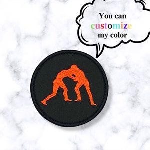 May include: Orange embroidered wrestling silhouette patch on a black circular background. The patch is approximately 2 inches in diameter.