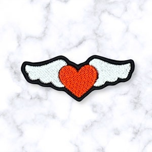 May include: A red heart with white wings, embroidered on a black fabric patch.