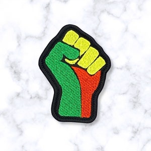 May include: A green, yellow, and red embroidered patch of a raised fist. The fist is a symbol of solidarity and strength.