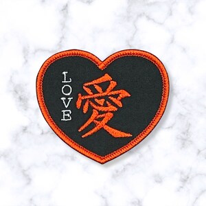 May include: Black heart-shaped patch with an orange embroidered Chinese character for "love" and the word "LOVE" vertically on the left side.