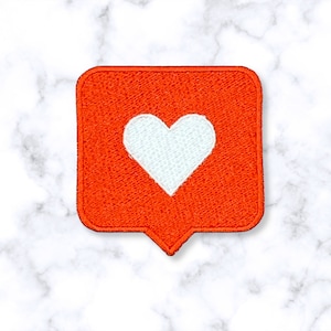 May include: A red square-shaped patch with a white heart in the center. The patch has a rounded bottom and looks like a social media notification icon.