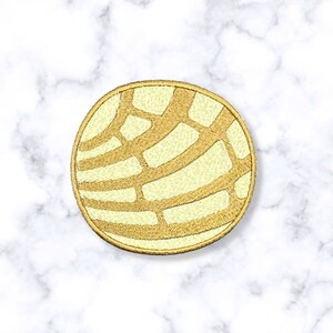 May include: A yellow and gold embroidered patch shaped like a round bread with a decorative pattern.