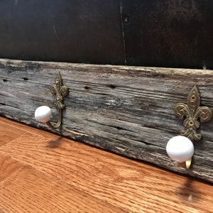 May include: A rustic wooden coat rack with three hooks. Each hook features a decorative fleur-de-lis design and a white ceramic knob.