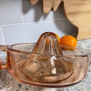 K&ouml;nnte beinhalten: Ein vintage rosa gl&auml;serner Zitruspresse mit geriffeltem Oberteil und breiter Basis. Die Presse ist aus Glas und hat eine strukturierte Oberfl&auml;che.