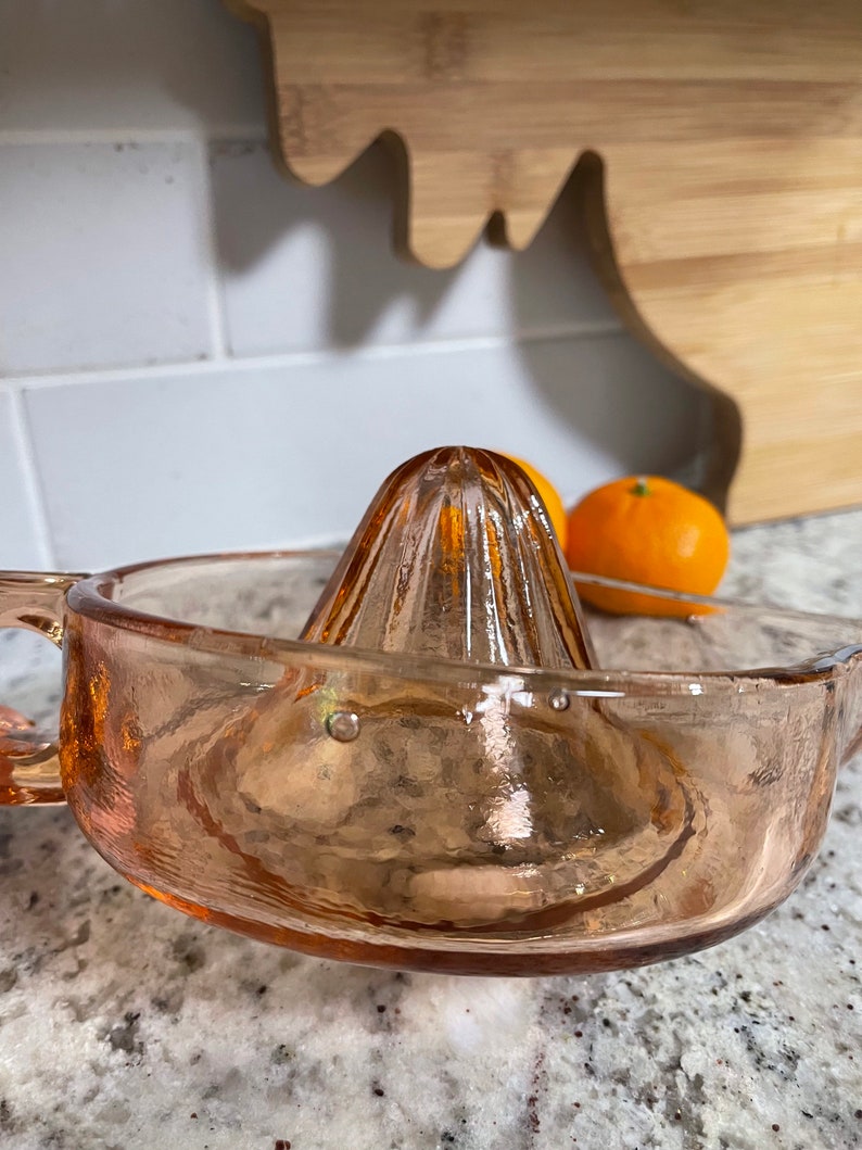 K&ouml;nnte beinhalten: Ein vintage rosa gl&auml;serner Zitruspresse mit geriffeltem Oberteil und breiter Basis. Die Presse ist aus Glas und hat eine strukturierte Oberfl&auml;che.