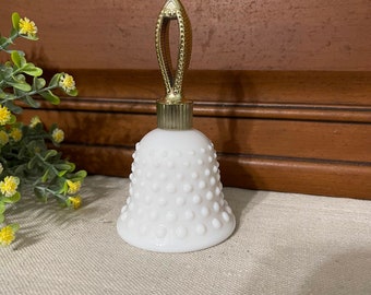 May include: A white milk glass bell-shaped bottle with a gold metal stopper. The bottle has a textured surface with small raised dots.
