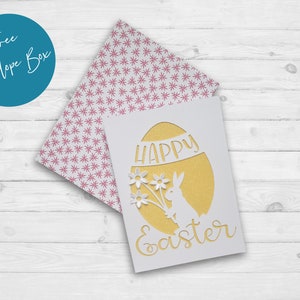 Puede incluir: Una tarjeta blanca con un huevo de purpurina dorada recortado. El huevo tiene las palabras "Feliz Pascua" escritas en su interior. Un conejito blanco con un ramo de flores est&aacute; recortado dentro del huevo.
