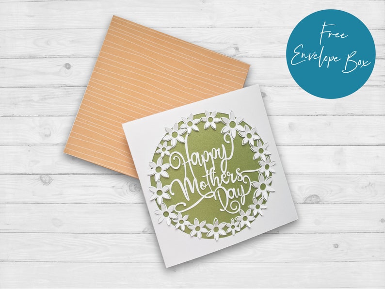 May include: A white card with a green circle and white flowers around the edge. The text "Happy Mother's Day" is written in white inside the circle.