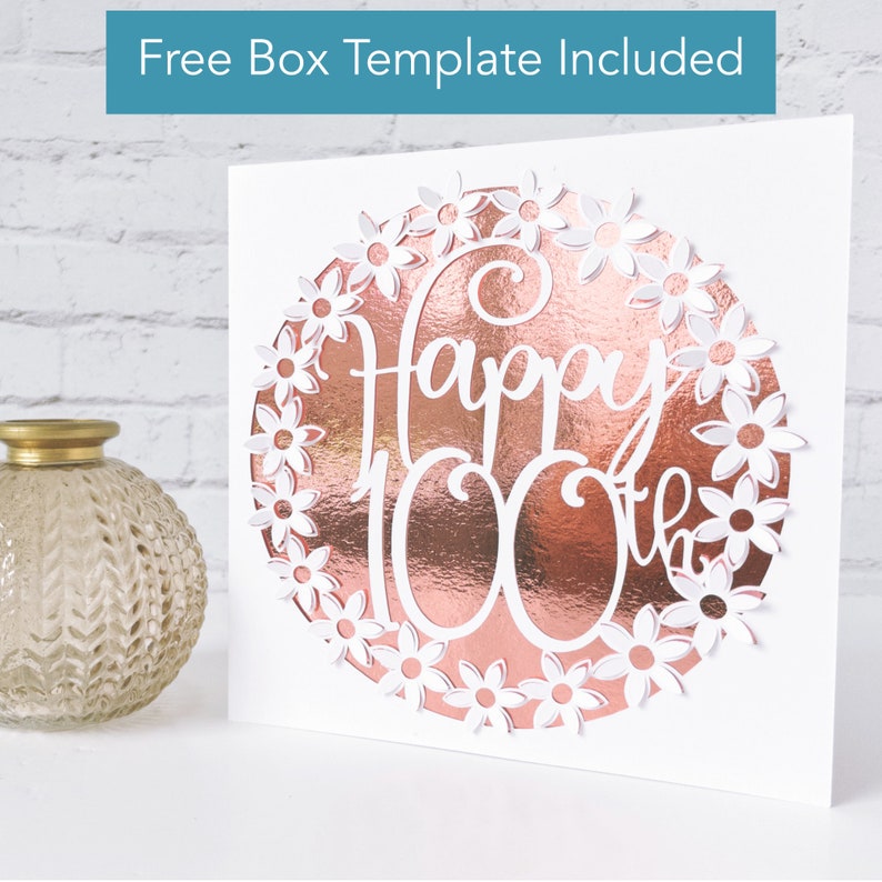 May include: A white card with a rose gold foil circle that says "Happy 100th" in white script. The circle is surrounded by white daisy cutouts. The text "Free Box Template Included" is at the top.