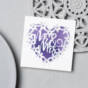Puede incluir: Tarjeta blanca con un dise&ntilde;o en forma de coraz&oacute;n morado con un borde floral blanco y el texto "Mr & Mrs" en escritura blanca.