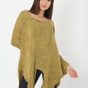 May include: Mustard yellow knit poncho sweater with a square neckline and asymmetrical hem. The long-sleeved top has ribbed detailing and a relaxed fit. The model is wearing dark blue jeans. A stylish addition to any wardrobe.