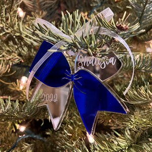 Op de afbeelding: Een transparante glazen kerstversiering in de vorm van een blauwe strik met de naam "Shalisia" en het jaar "2022" erop gegraveerd.