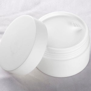 Può includere: Barattolo di plastica bianco con un coperchio. Il barattolo è aperto e il coperchio è di lato. Il barattolo è vuoto.