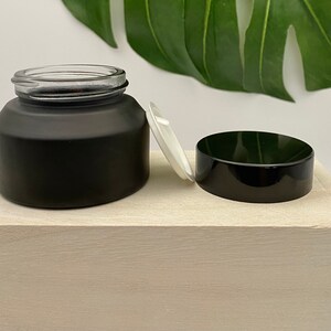 K&ouml;nnte beinhalten: Ein schwarzes, mattes Glasgef&auml;&szlig; mit einem schwarzen Deckel und einem wei&szlig;en Plastikdeckel. Das Gef&auml;&szlig; steht auf einer wei&szlig;en Holzoberfl&auml;che.