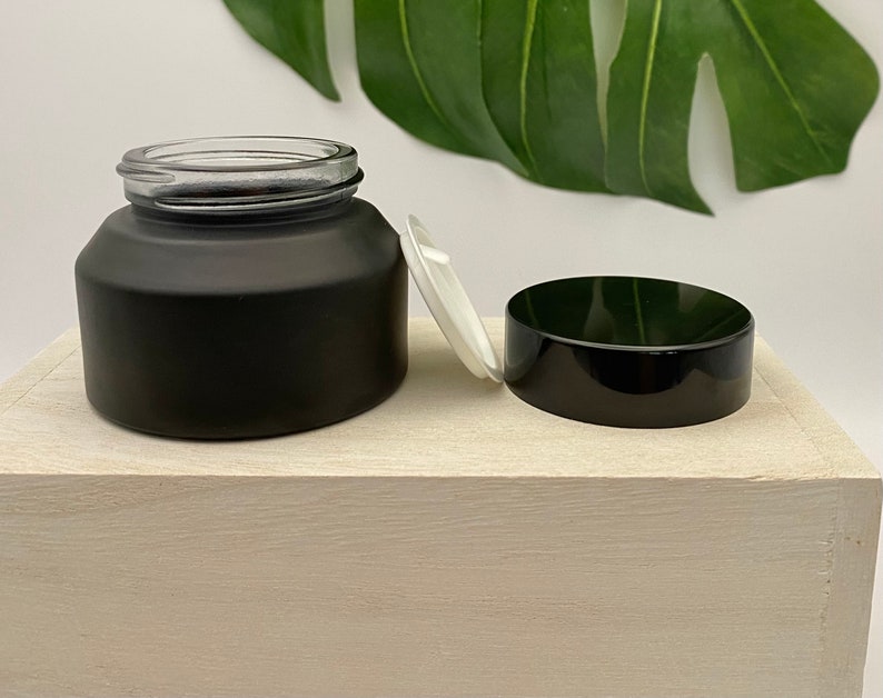 K&ouml;nnte beinhalten: Ein schwarzes, mattes Glasgef&auml;&szlig; mit einem schwarzen Deckel und einem wei&szlig;en Plastikdeckel. Das Gef&auml;&szlig; steht auf einer wei&szlig;en Holzoberfl&auml;che.