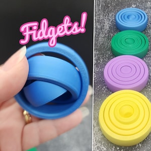 Puede incluir: Un conjunto de cuatro juguetes sensoriales, cada uno con un color y un número de anillos diferentes. Los colores son azul, verde, morado y amarillo. Los juguetes están hechos de plástico y están diseñados para girar y voltear.