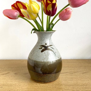 Puede incluir: Un ramo de tulipanes rosas, amarillos y rojos en un jarrón de cerámica marrón y blanco con un diseño marrón.