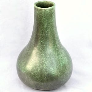 May include: A green ceramic vase with a speckled texture. The vase has a rounded base that tapers to a narrow neck and opening. The color is a blend of green hues, with a subtle sheen. The vase is a decorative item.
