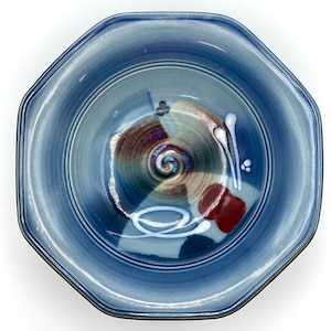 May include: A blue ceramic bowl with a decorative design featuring swirls, lines, and a red accent. The bowl has an octagonal shape and a glazed finish.