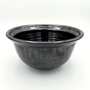 May include: A black ceramic bowl with a textured, ribbed design around the rim. The bowl has a glossy finish and a rounded shape.