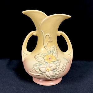 May include: A vintage yellow vase with a pink base and handles. The vase features a floral design with a yellow centre and light blue and white petals. The vase has a unique shape with two flared openings.