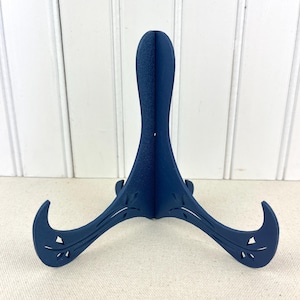 May include: A blue ceramic display stand with a decorative cut-out design. The stand has three legs and is designed to hold a plate or other object.