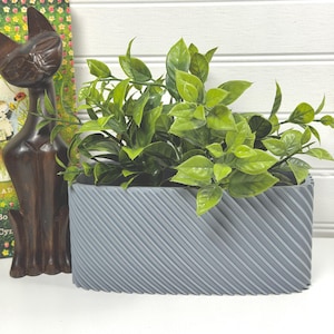 Vaso retangular arredondado com nervuras finas, baixo, para plantas, ideal para ambientes internos ou como floreira de mesa.