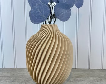 May include: A beige ceramic vase with a swirling, ribbed design. The vase is empty and has a rounded bottom.